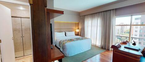Une chambre d’hôtel avec un lit, un bureau, une chaise, une fenêtre avec des rideaux et une vue sur les bâtiments environnants.