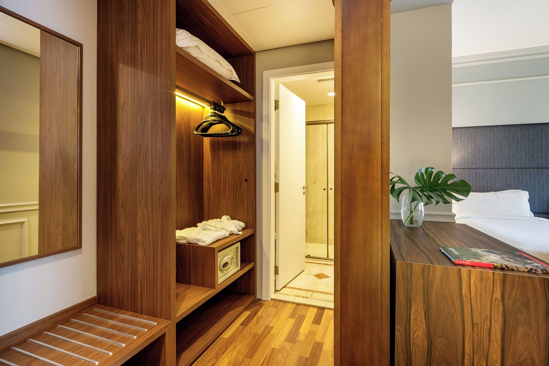 Een hotelkamer met een houten garderobe, een nachtkastje met een plant, een bed en een douche.
