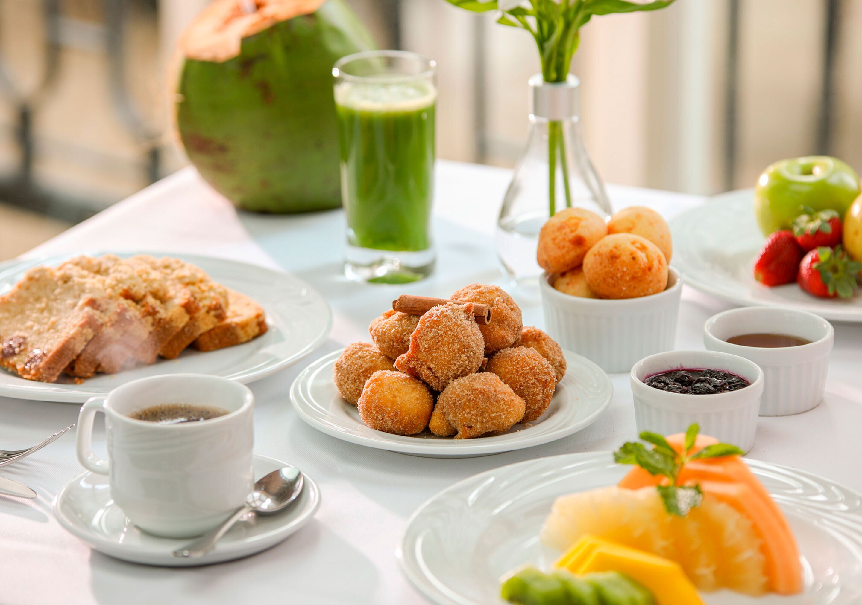 Una mesa de desayuno con cruasanes, fruta, un batido verde y café.