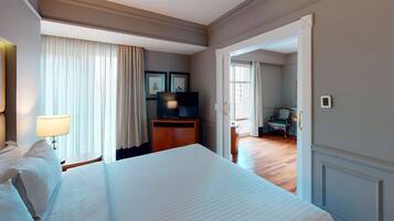Una habitación de hotel con una cama grande, un escritorio con televisión y una puerta que da a otra habitación.