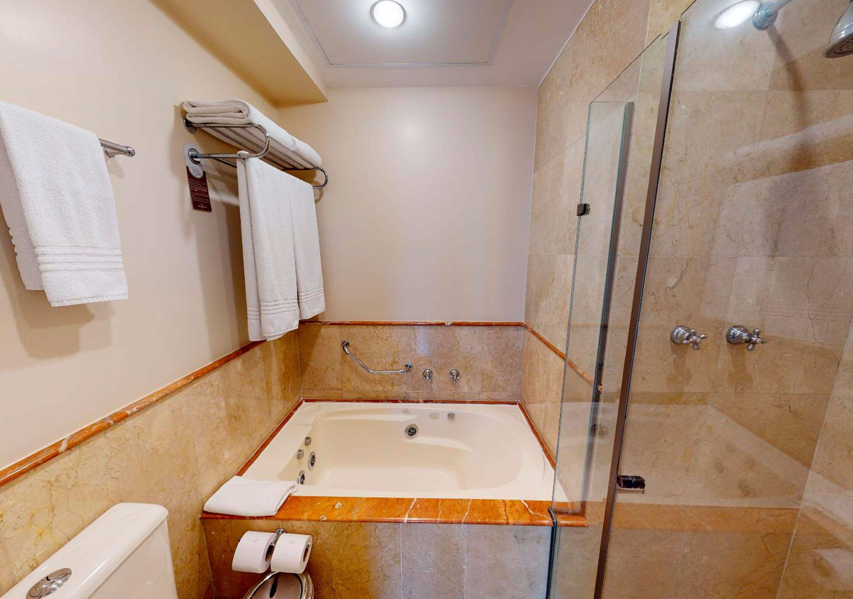 Un baño con bañera, inodoro, ducha y cabina de ducha con paredes de vidrio.