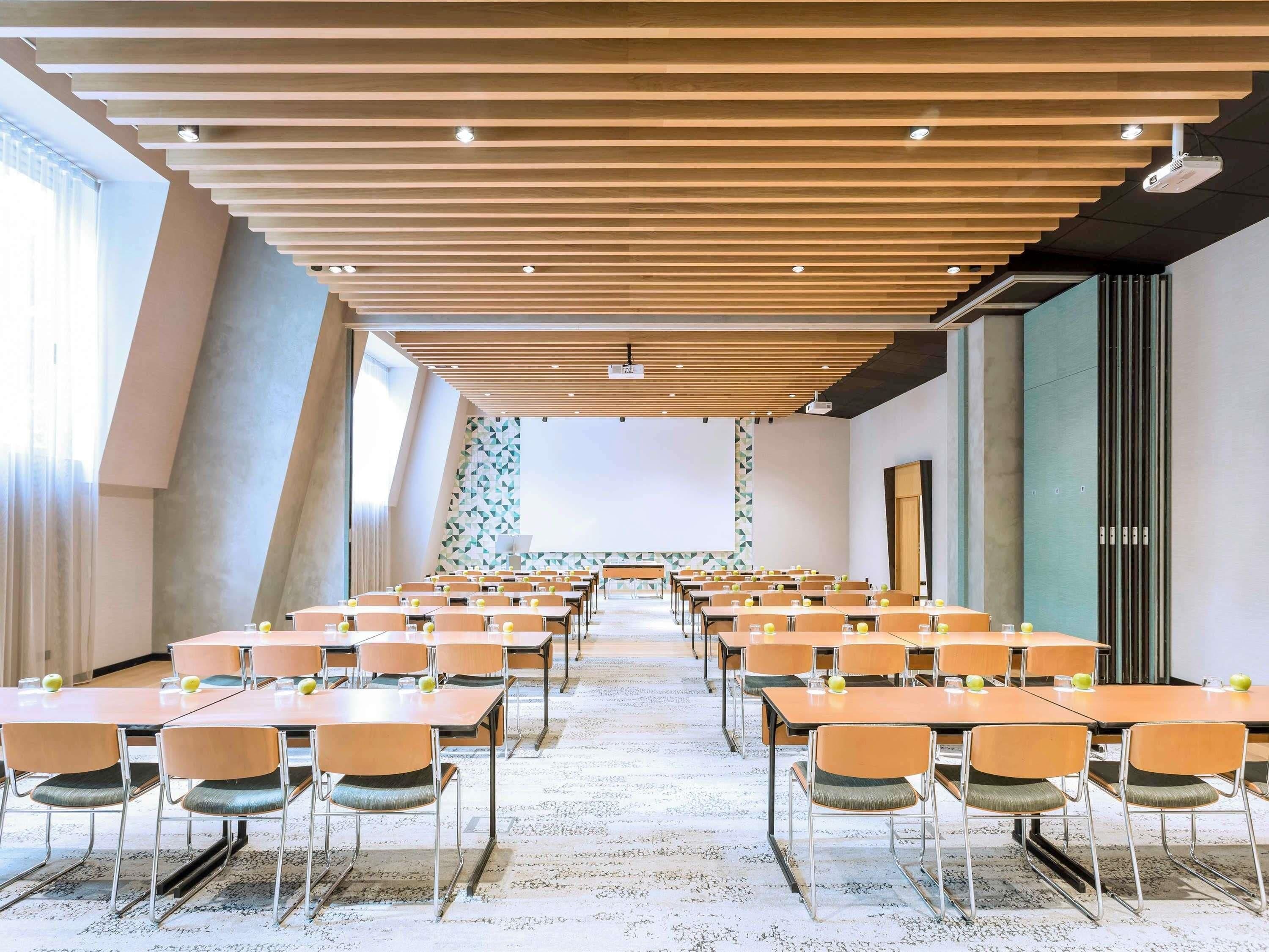 A conference room with long tables and chairs, a projector, and a large screen.