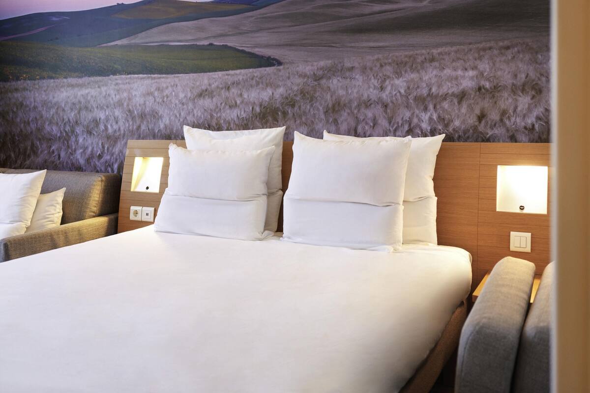 A hotel room with a large bed, two bedside tables, and a view of rolling hills.