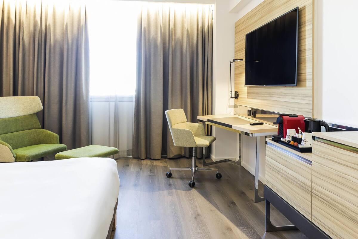 A hotel room with a bed, a desk, a chair, a TV, and a coffee machine.
