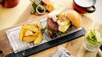 Comida con una hamburguesa, papas fritas y una bebida sobre una mesa de madera, con periódicos debajo.