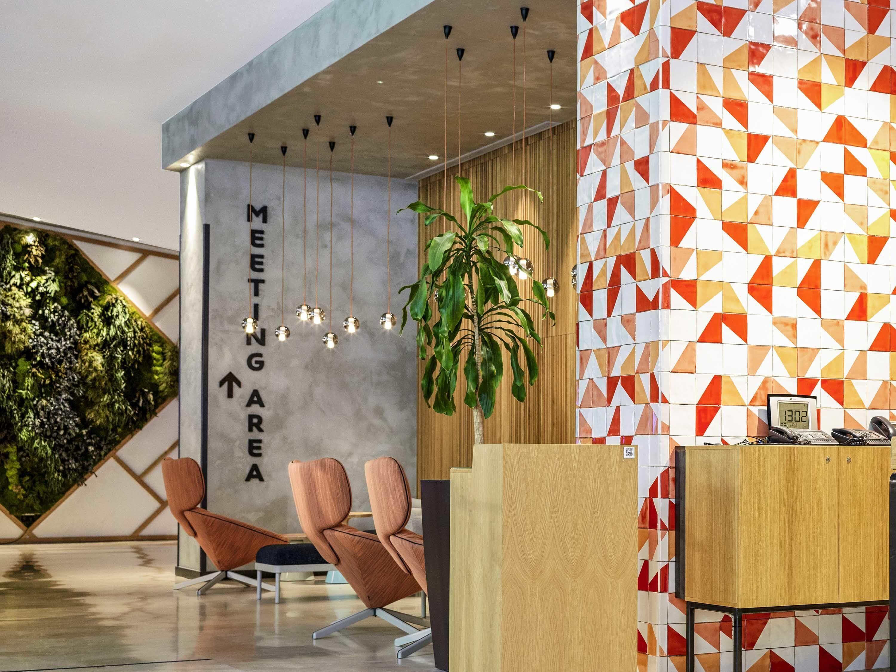 A modern reception area with a 'MEETING AREA' sign, a reception desk, two chairs, a hanging plant, and a geometric patterned wall.