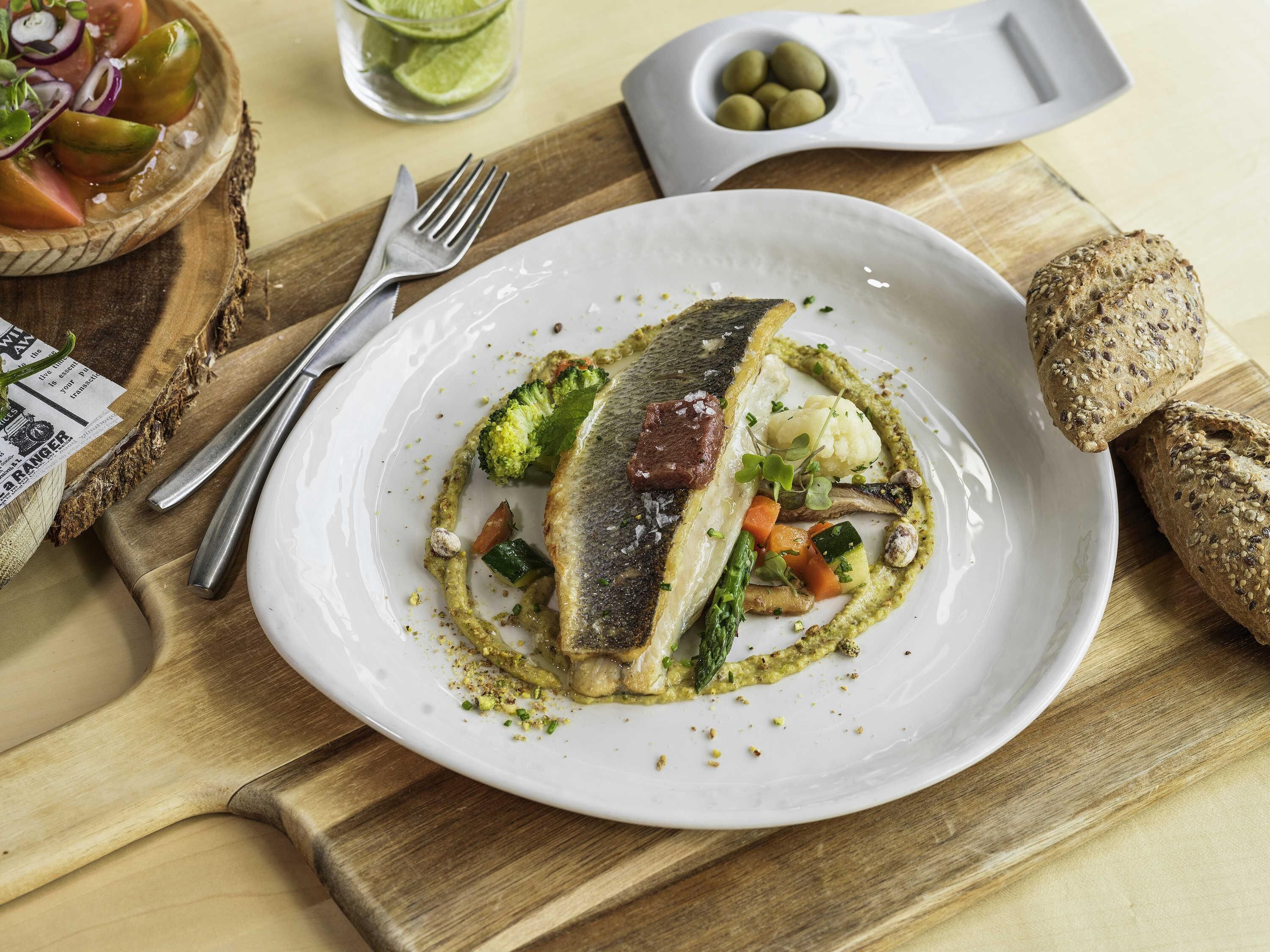 A plate of fish with vegetables and a side of bread on a wooden table.