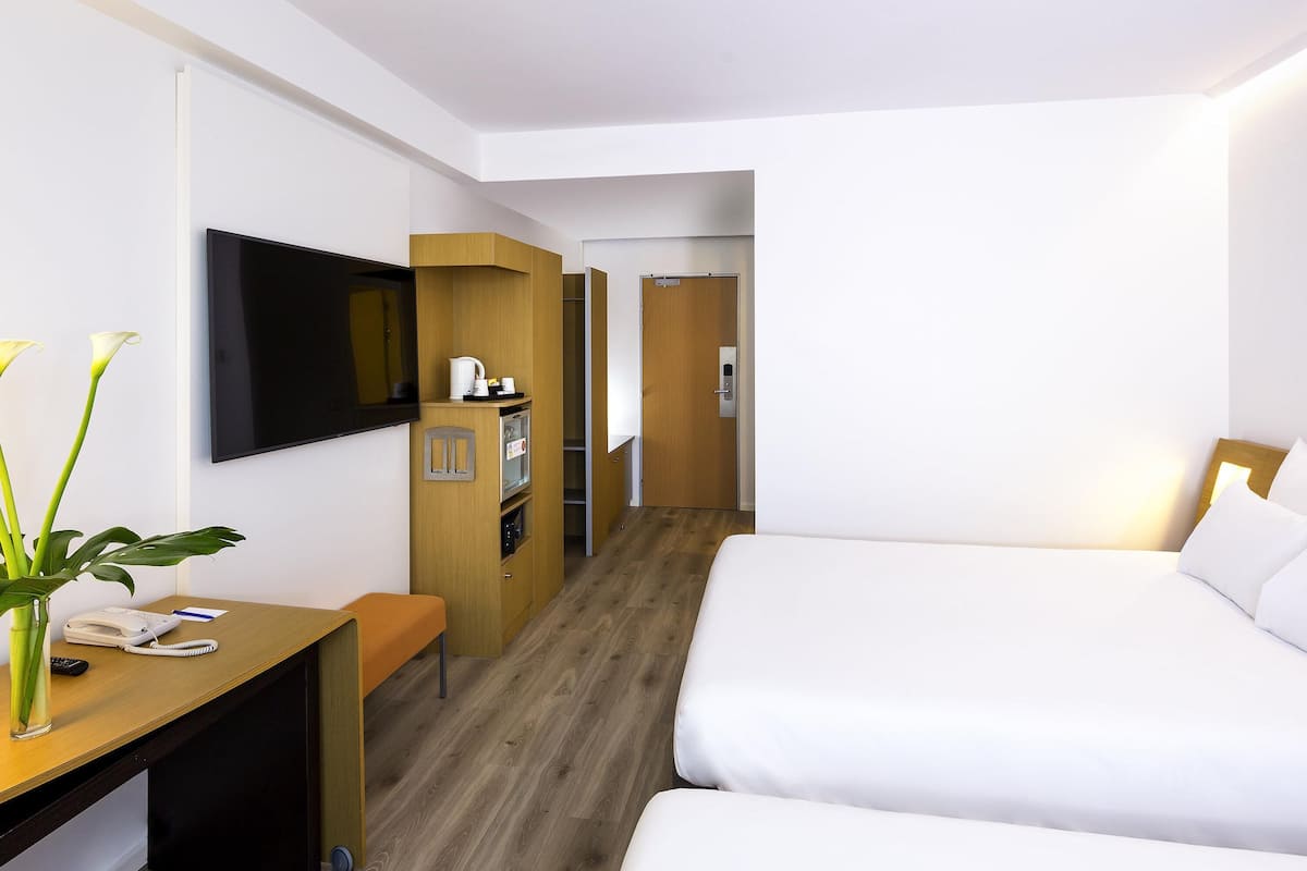 A hotel room with a bed, a desk with a telephone, a television, and a small kitchenette.