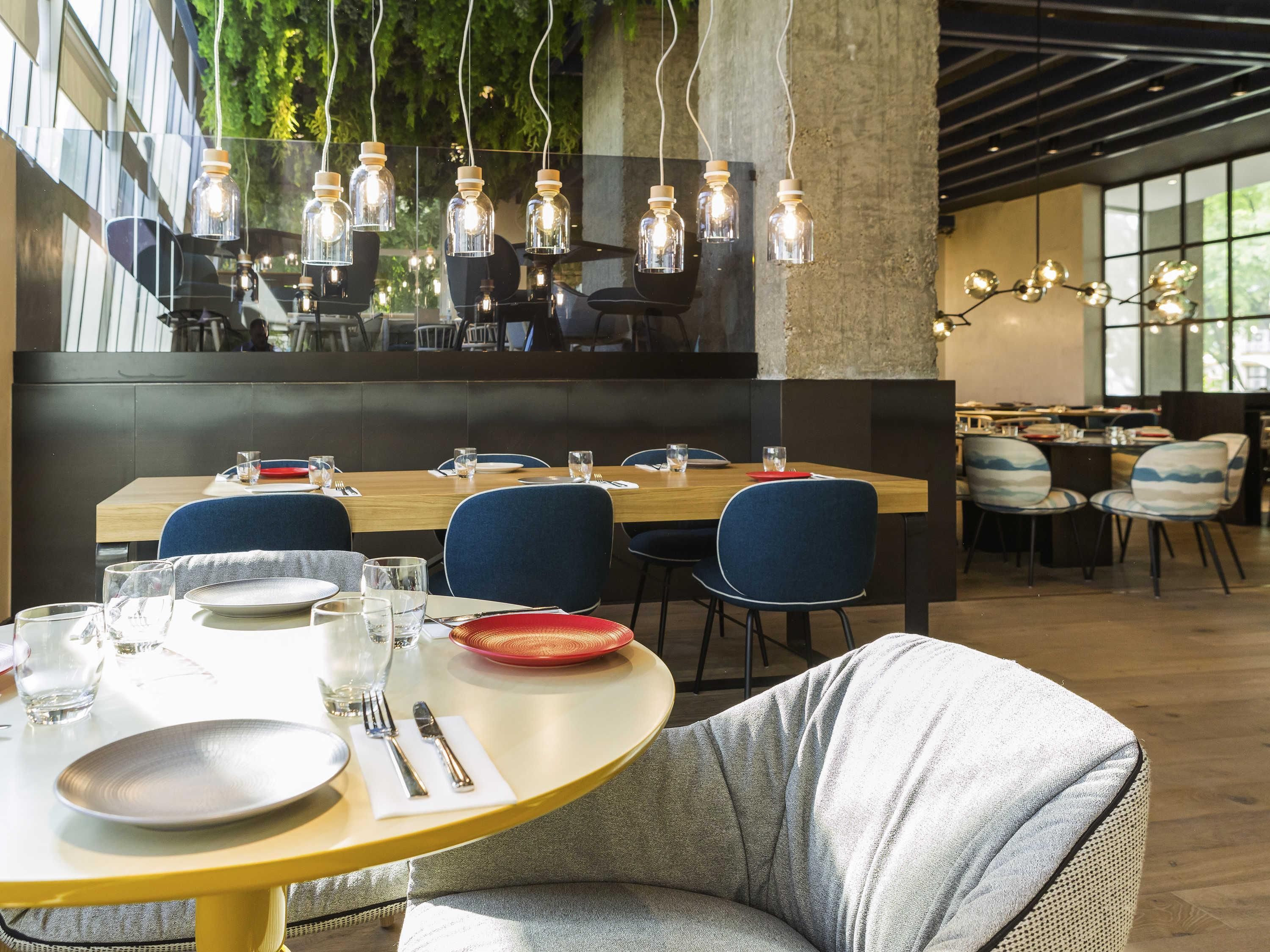 Un restaurante con mesas redondas, sillas, lámparas colgantes y vistas a zonas verdes.