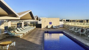 A rooftop pool area with lounge chairs and a table, surrounded by a wooden deck. - Novotel Sevilla (Seville)