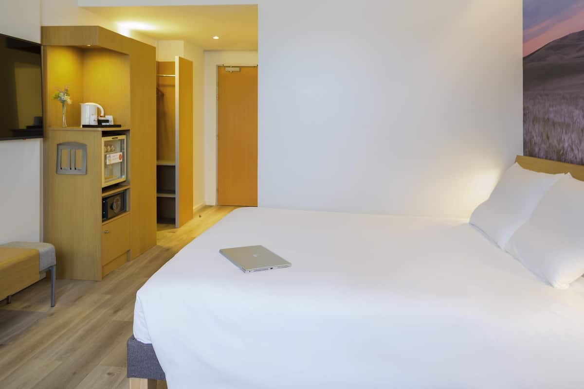 A hotel room with a bed, a desk with a laptop, a wardrobe, and a small kitchenette.