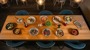 A dining area with a long wooden table set for a meal, surrounded by chairs, and illuminated by hanging light fixtures. - Novotel Sevilla (Seville)