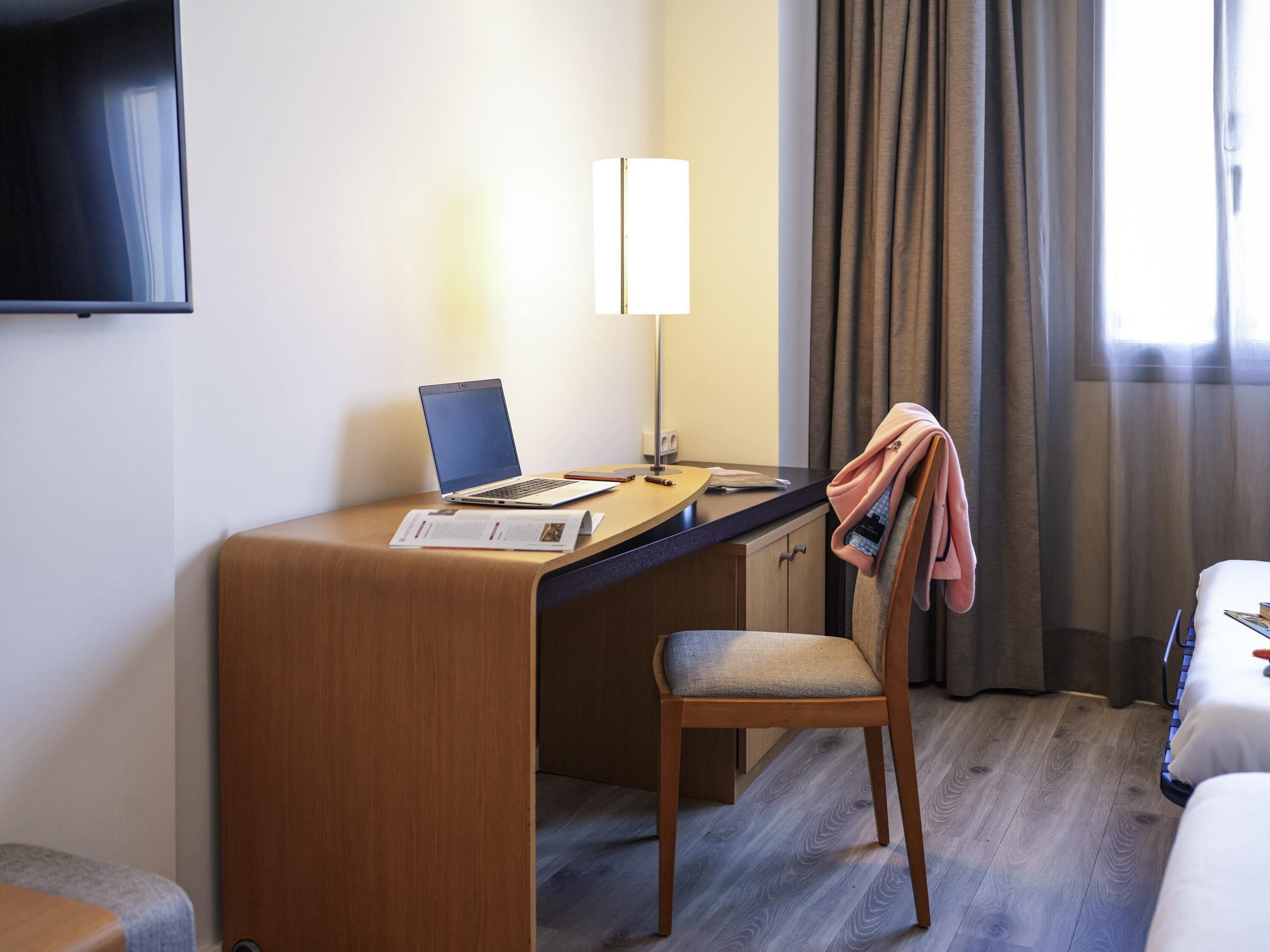 Une chambre d’hôtel avec un bureau en bois, un ordinateur portable, une lampe, une chaise et un lit.