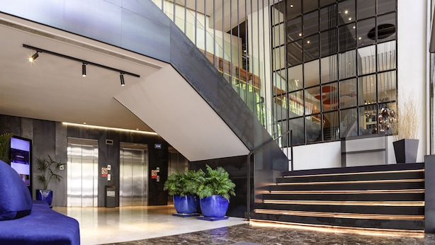 A modern lobby with a staircase, elevators, and large potted plants. - Novotel Sevilla (Seville)