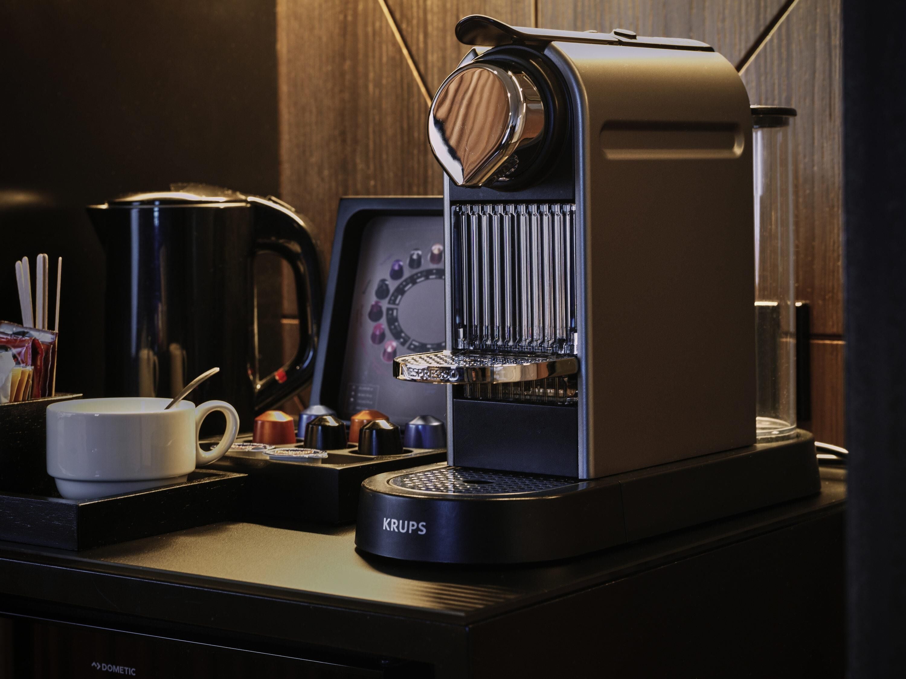Une machine à café Krups posée sur un plan de travail, avec une tasse blanche, une cafetière et un moulin à café.