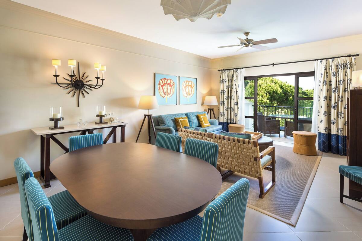 A dining area with a round table and blue-striped chairs, a sofa with cushions, and a ceiling fan.