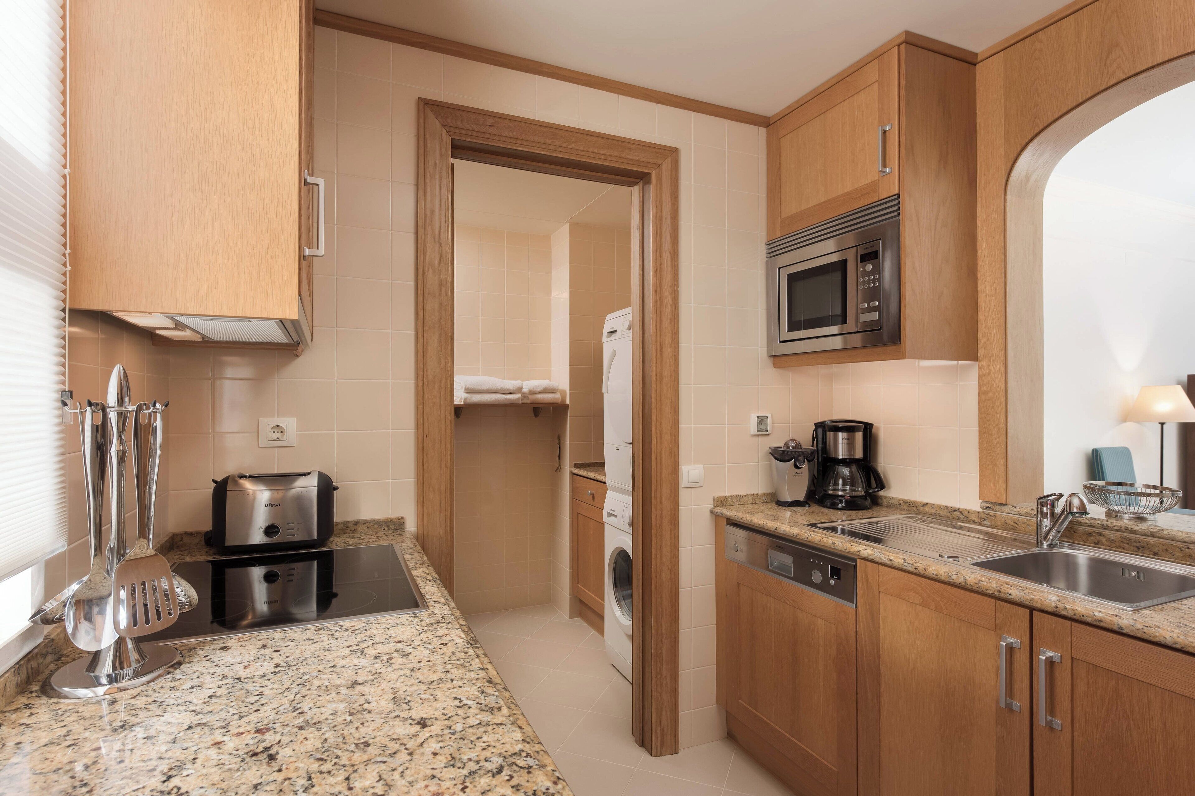 A modern kitchen with wooden cabinets, a stainless steel sink, a microwave, and a coffee maker.