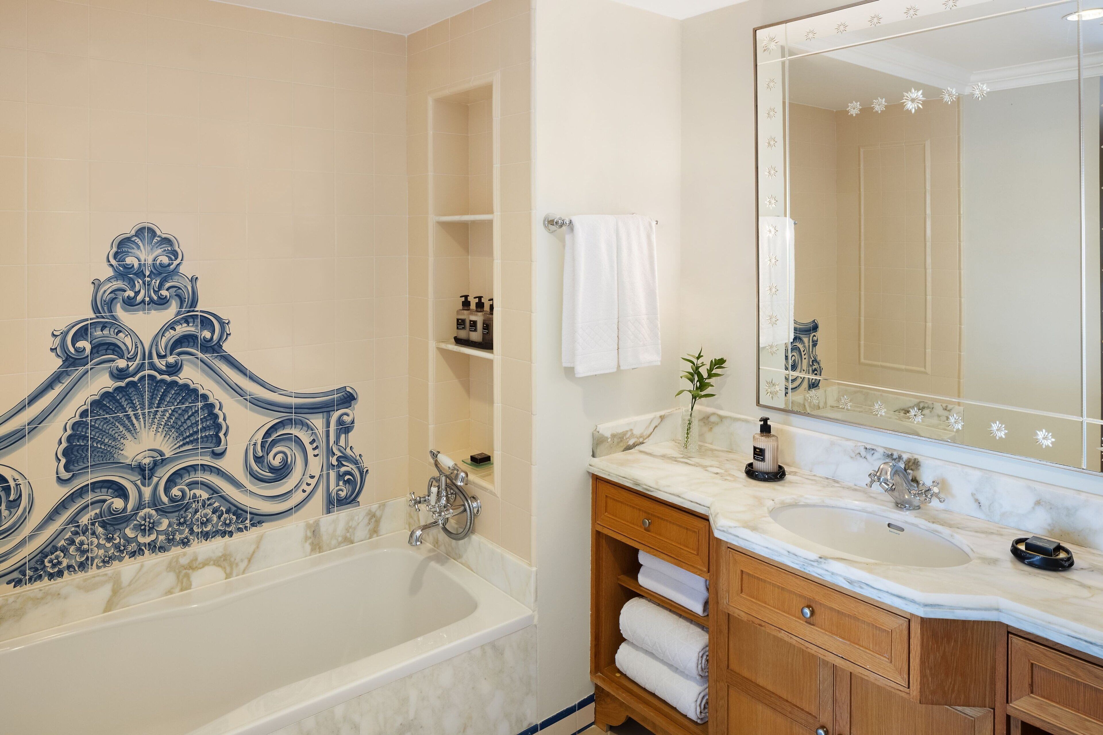 A bathroom with a bathtub, a large mirror, a vanity with a sink, and a shelf with toiletries.
