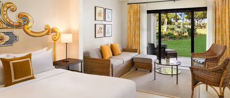 A hotel room with a large bed, a sofa, a chair, a small table, and a view of the outdoors through a sliding door.