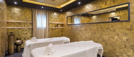 A spa room with two massage tables, a large mirror, and a decorative ceiling light.