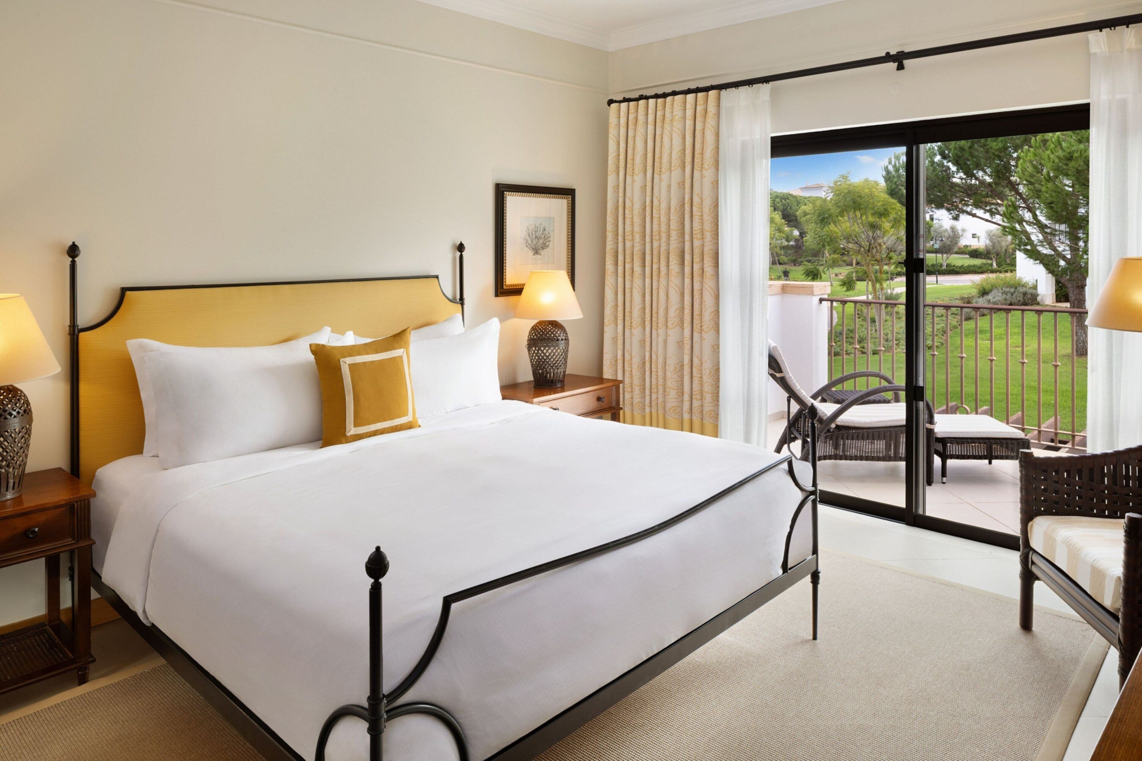 A hotel room with a large bed, two bedside tables with lamps, a chair, and a view of the garden through a sliding glass door.