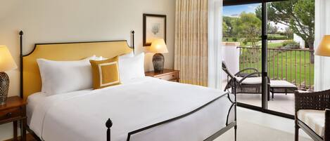A hotel room with a large bed, two bedside tables with lamps, a chair, and a view of the garden through a sliding glass door.