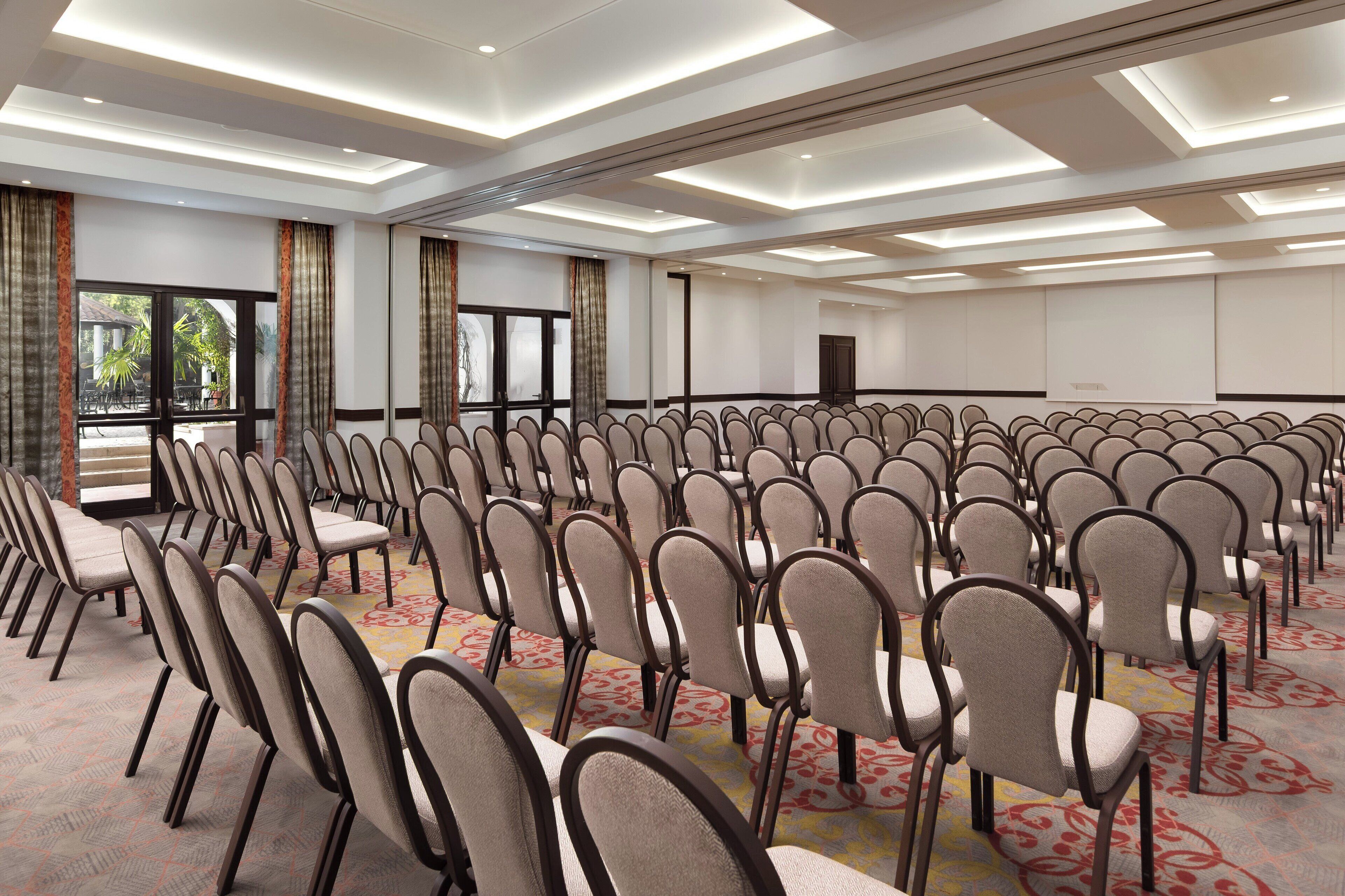 Een congrescentrum met rijen stoelen, grote ramen en een vloerbedekking.
