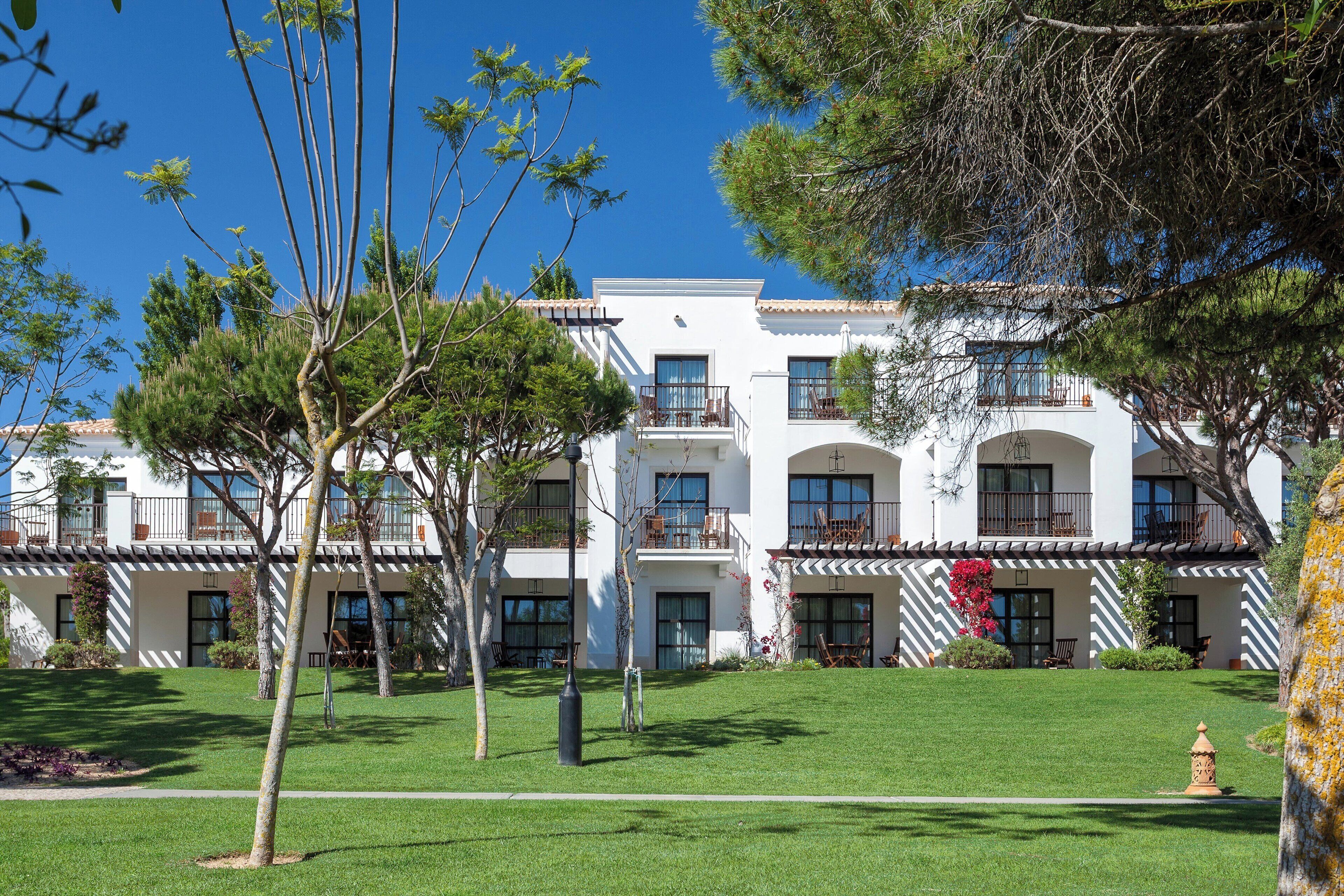 A multi-story hotel with a white facade, balconies, and a well-maintained lawn.