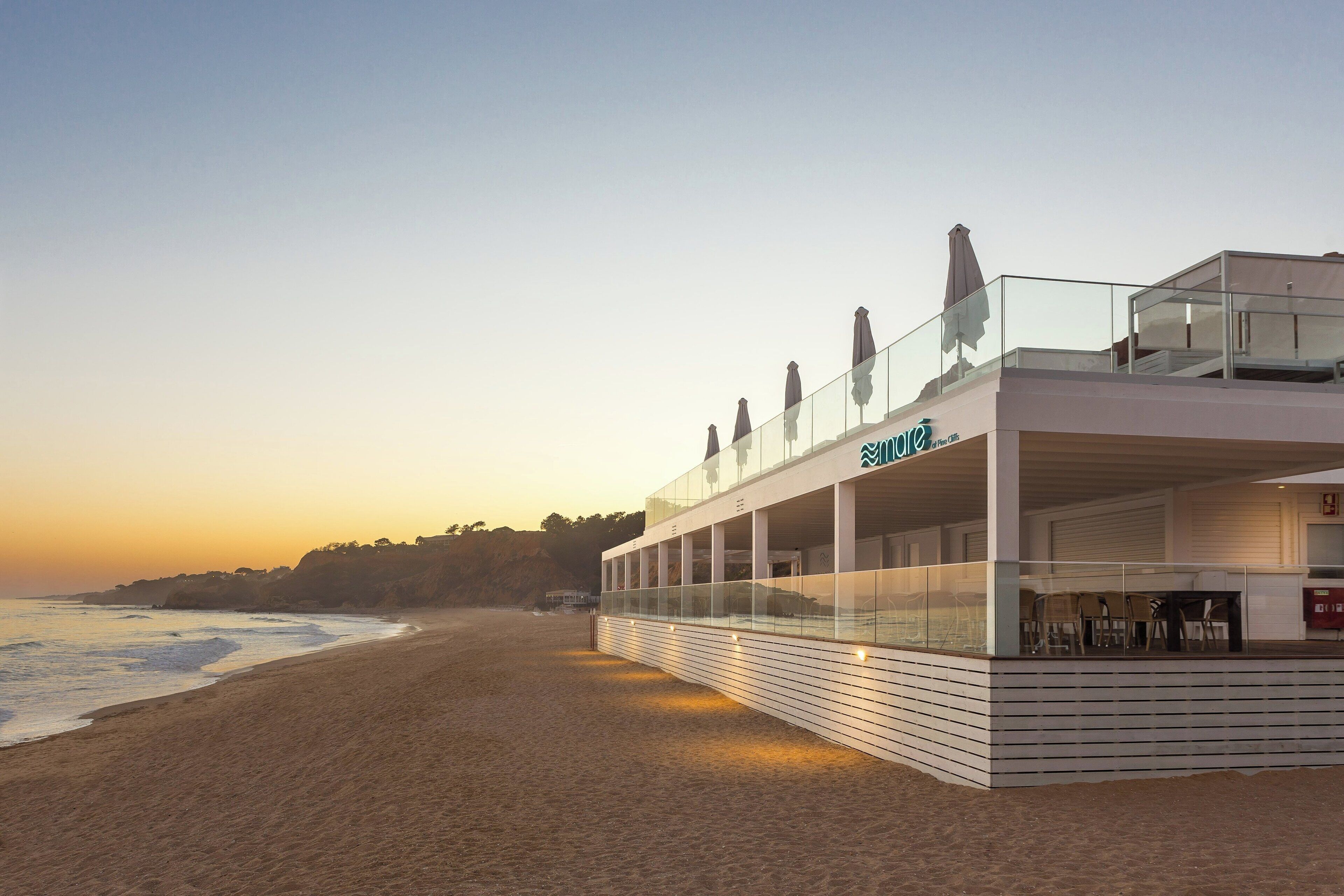A beachfront hotel with a glass railing overlooking the ocean, a covered seating area, and a sign indicating the name 'Blue House'.