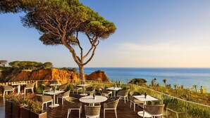Un espace de restauration en plein air, avec des tables et des chaises, offrant une vue sur un paysage côtier caractérisé par des falaises et la mer.