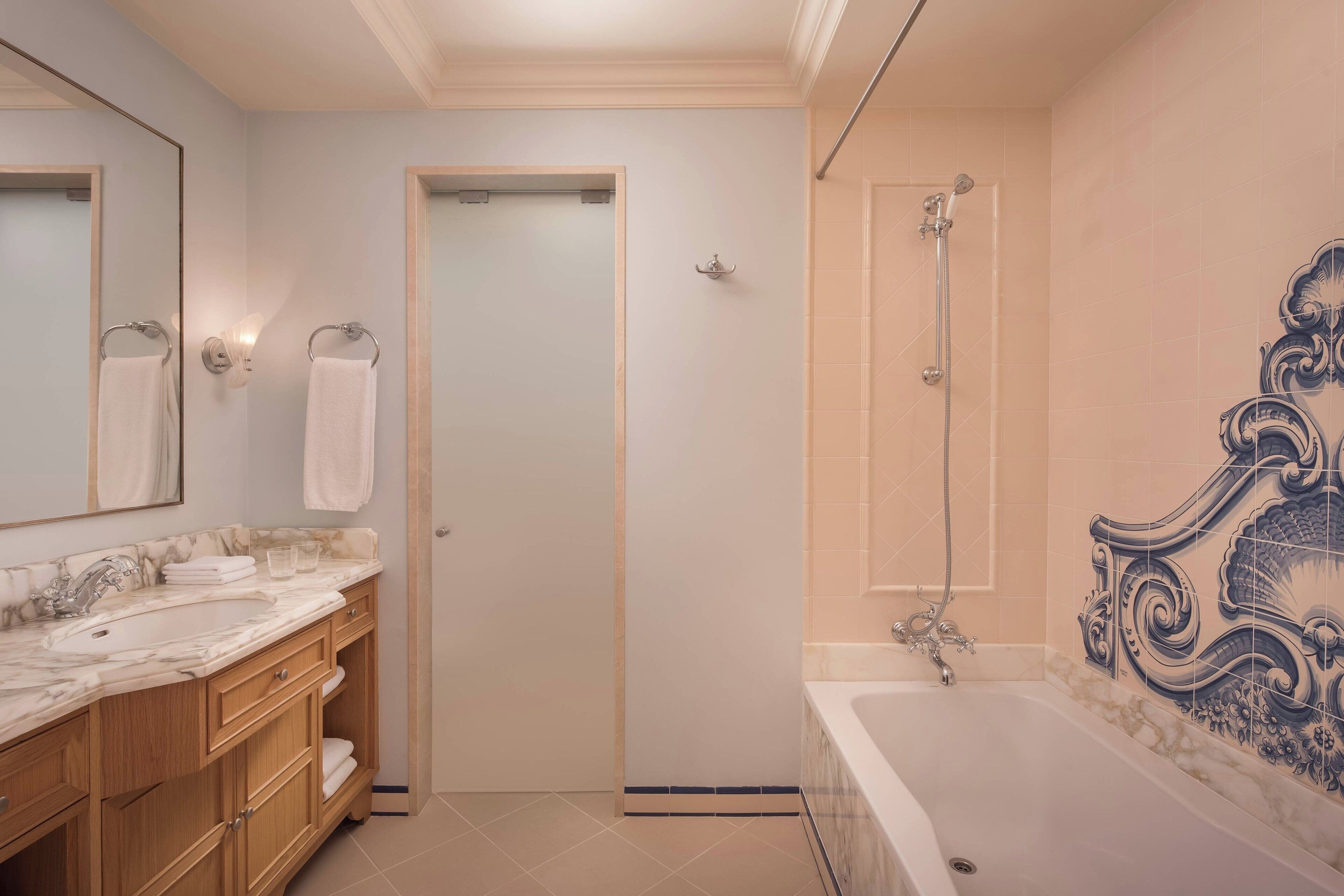 Un baño con lavamanos de mármol, tocador de madera, bañera con pared de azulejos decorativos y zona de ducha.