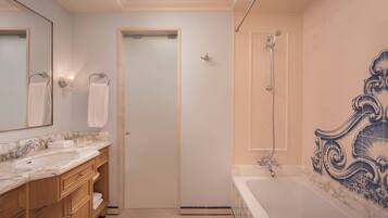 Un baño con lavamanos de mármol, tocador de madera, bañera con pared de azulejos decorativos y zona de ducha.