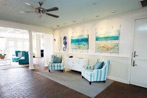 A spacious lobby with a brick floor, two striped armchairs, a white console table, and a ceiling fan.