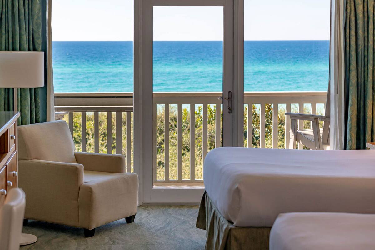 A hotel room with a balcony overlooking the ocean, a bed, a chair, and a dresser.