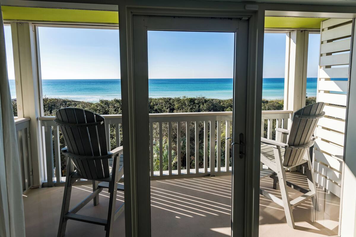 A balcony with two Adirondack chairs facing a view of the ocean.