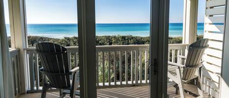 A balcony with two Adirondack chairs facing a view of the ocean.
