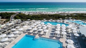 A resort pool area with multiple lounge chairs and umbrellas, a large central pool, and a beach in the background. - WaterColor Inn & Resort (Santa Rosa Beach)