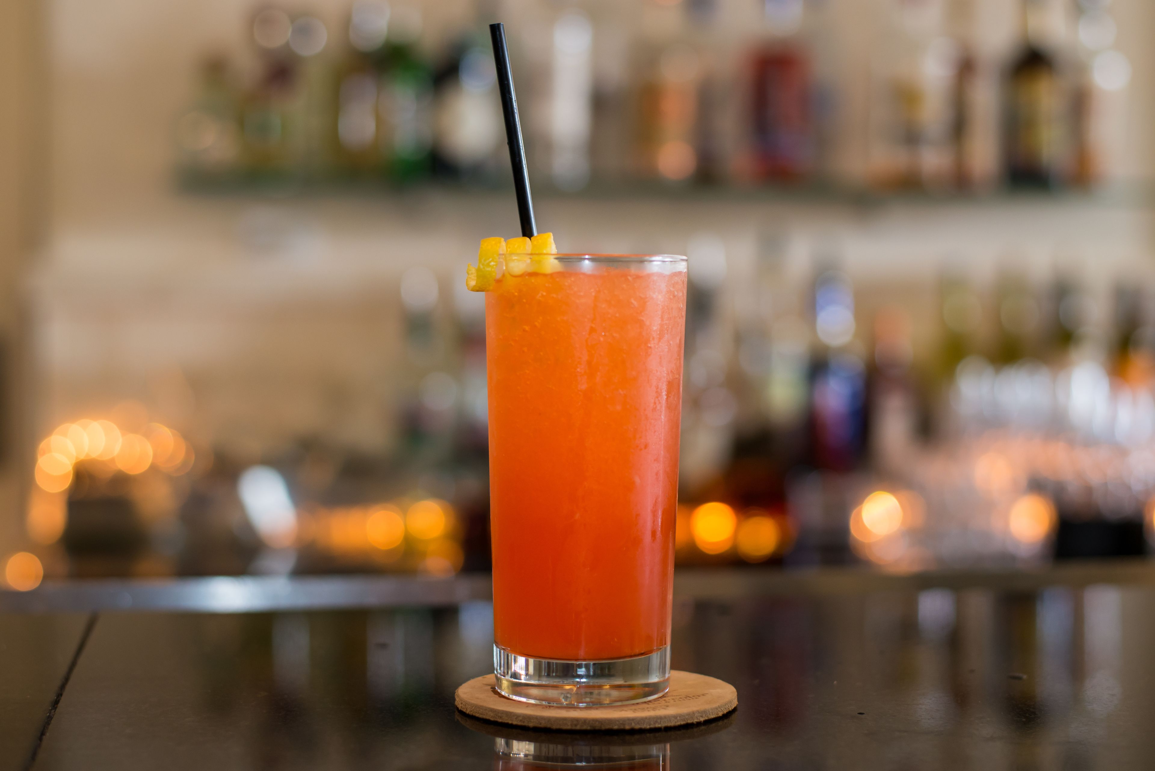 Un grand verre de boisson à l’orange, avec une paille et une tranche de fruit posée sur un dessous de verre.