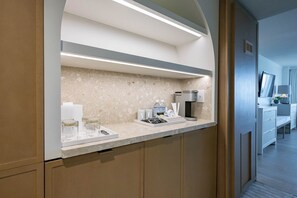 A modern hotel reception area with a marble countertop, a coffee machine, and a seating area with a TV and lamp.