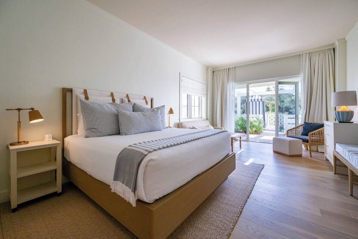 A spacious bedroom with a large bed, bedside tables, a desk, and a view of the outdoors.