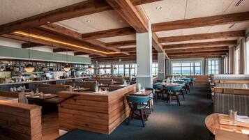 A spacious restaurant with wooden beams, blue seating, and a view of the ocean.