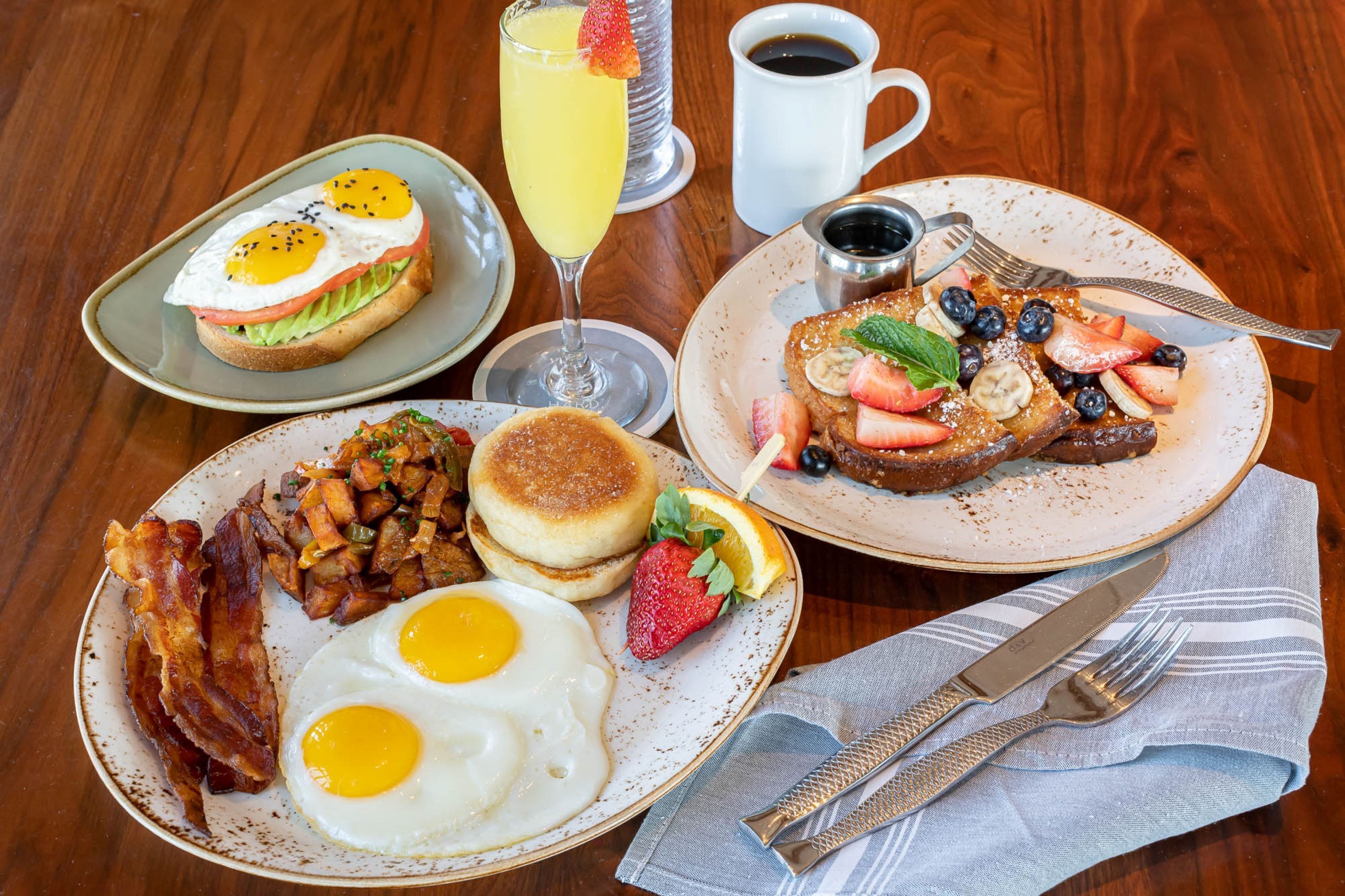 A breakfast spread with eggs, bacon, pancakes, and fruit on plates.