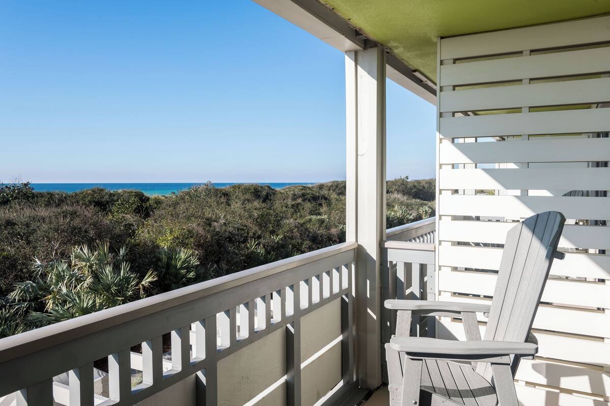 A balcony with a view of the ocean, a white chair, and a railing.
