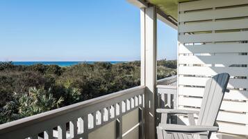 A balcony with a view of the ocean, a white chair, and a railing.