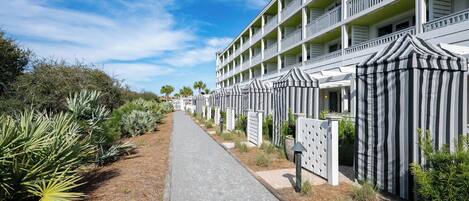 A hotel with a long, straight pathway leading to the entrance, flanked by rows of palm trees and a building with multiple balconies.