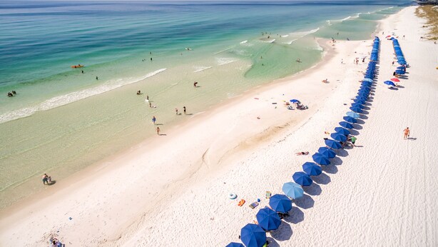 A beach with clear turquoise waters, a sandy shore, and a row of blue umbrellas. - WaterColor Inn & Resort (Santa Rosa Beach)