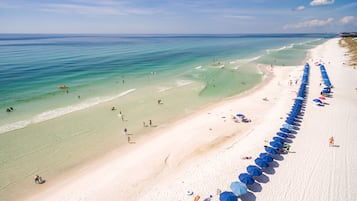 Na praia, areia branca, espreguiçadeiras, guarda-sóis