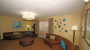Una sala de estar con un sofá y un sillón de cuero marrón, un reposapiés redondo y un cuadro grande en la pared.