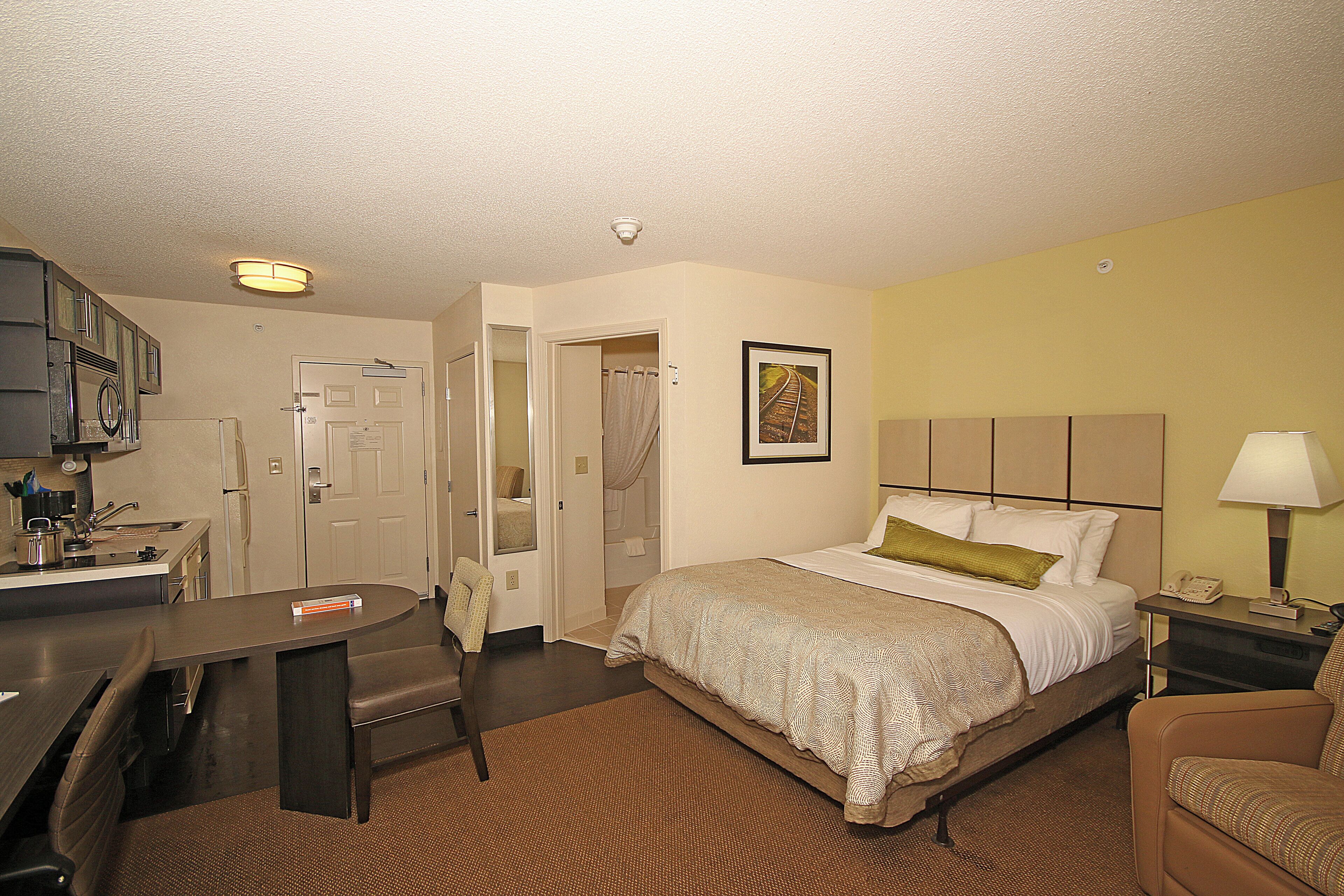 A hotel room with a bed, a desk, a chair, a bathroom, and a picture on the wall.