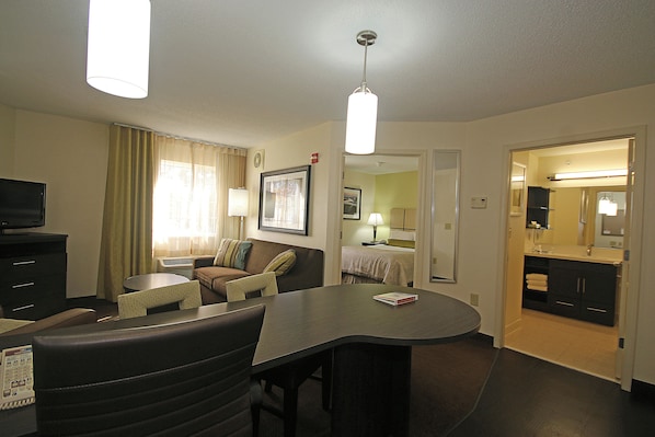Habitación de hotel con una mesa de comedor, un sofá, un televisor y una zona de cocina.